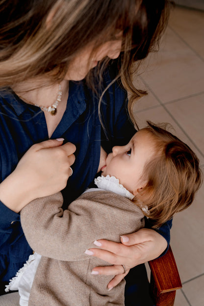 Jeune maman qui allaite discrètement grâce à sa Robe maternité pour les mamans ou future maman. Sa coupe polyvalente permet de porter la robe maternité pendant la grossesse et l'allaitement. Sa coupe évasée bohème donne un look chic et élégant. Sa matière en double gaze de coton apporte confort et style. Ses ouvertures de chaque côté de la poitrine permettent un accès facilité pour nourrir et allaiter son bébé rapidement, facilement et même discrètement.