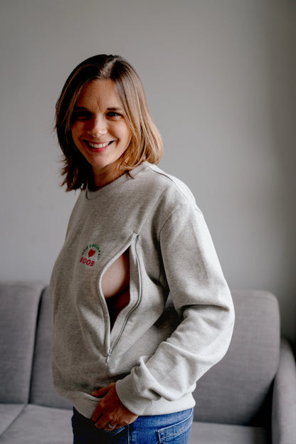 maman qui ouvre son sweat maternité gris chiné en coton, brodé au coeur "Mon Coeur fait boob". Sweat d'inspiration des années 90s, est polyvalent et peut être porté par les futures mamans enceinte pendant leur grossesse et aussi après l'accouchement pour allaiter bébé. Deux zips de la marque YKK de chaque côté de la poitrine permettent d'accéder au sein et de nourrir facilement, simplement et discrètement votre bébé. Un sweat moderne, tendance grâce à sa coupe loose confortable féminine