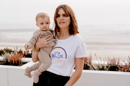 Maman qui porte son bébé dans les bras. avec en T-shirt allaitement 100% coton, avec des ouvertures avec zips pour allaiter facilement et discrètement. design "over the rainboob".