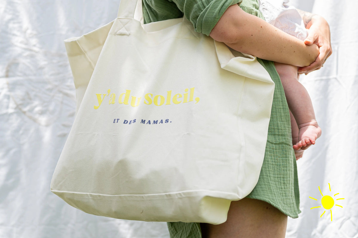 Sac à Langer  ou cabas XXL LIMKY. Ce fourre-tout 100% twill de coton est printé "Y'a du Soleil et des Mamas" pour un joli jeu de mot ensoleillé et vous accompagner pour toutes vos sorties : plage, bureau, ville, parc. Son format XXL permet à ce sac de contenir tous vos essentiels et indispensables de jeune maman de bébé.